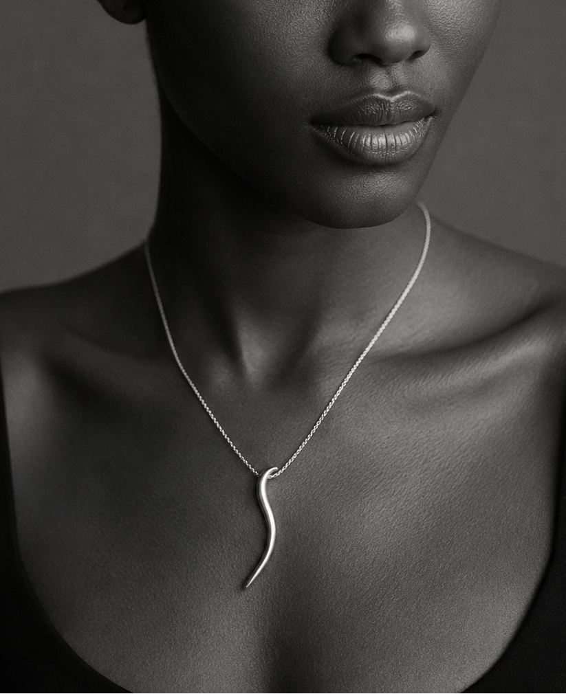 A black and white portrait of a woman wearing a delicate silver pendant necklace with a curved, organic shape.