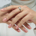 Close-up of hands with pink nail polish and a silver ring on a white background