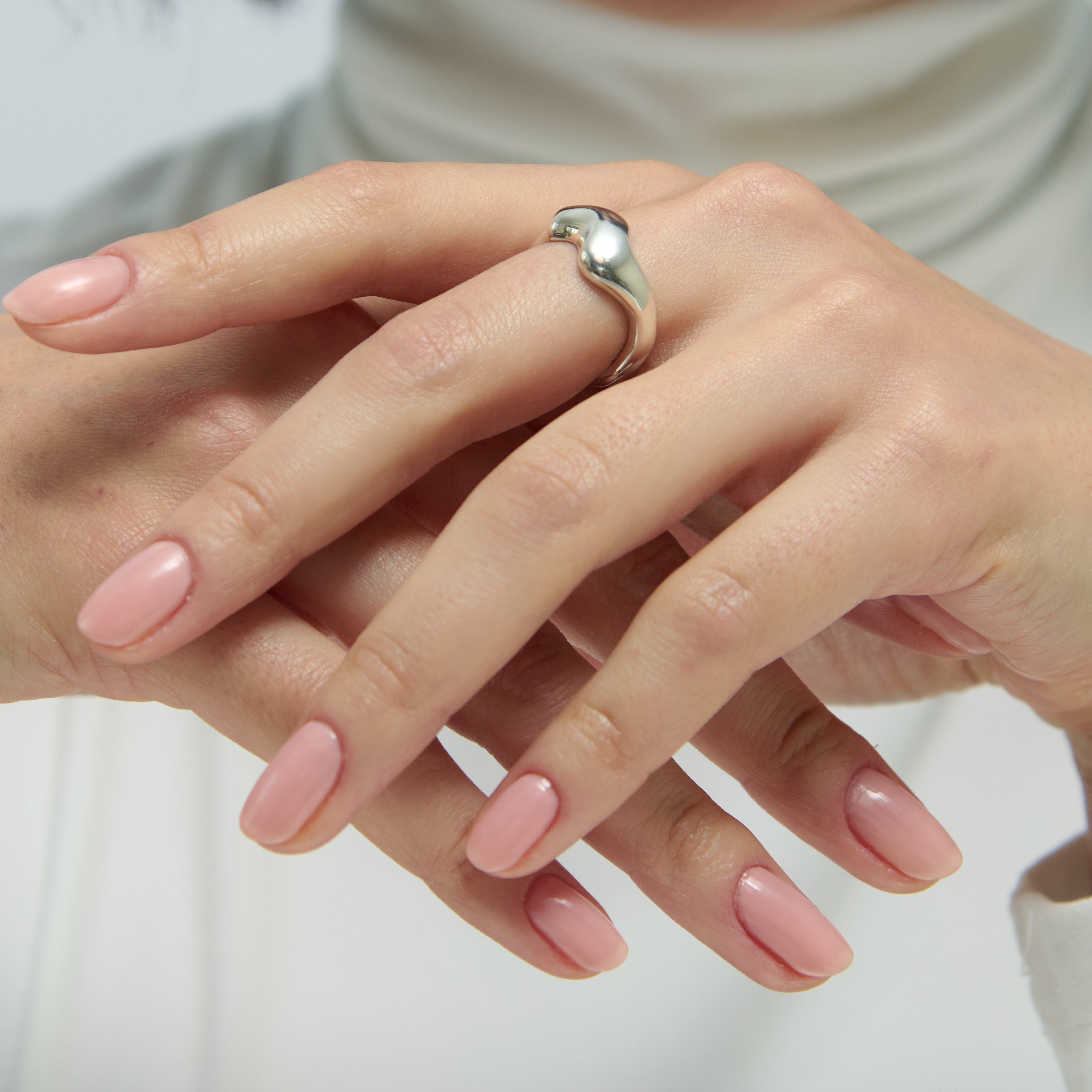 Close-up of hands with pink nail polish and a silver ring on a white background
